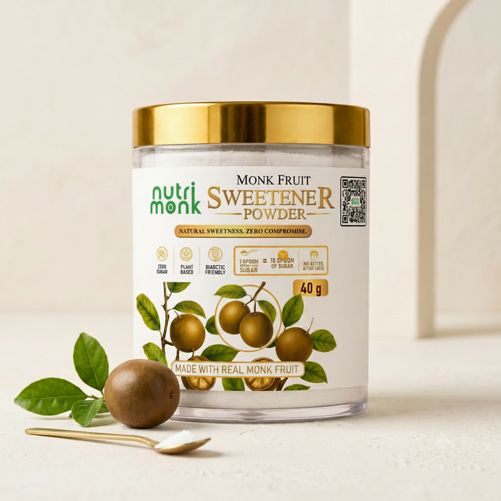 A jar of Nutri Monk Sweetener Powder with a gold lid and white label, styled on a light beige surface with a gold spoon and a real monk fruit and leaf in the foreground.